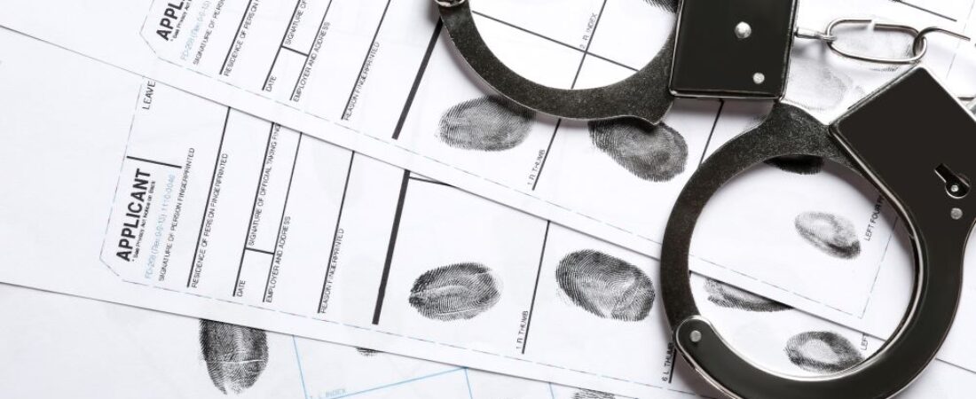 Criminal records with fingerprints and handcuffs on top of files.