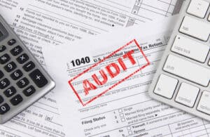 tax filings that have fraud stamped on them next to a calculator and computer