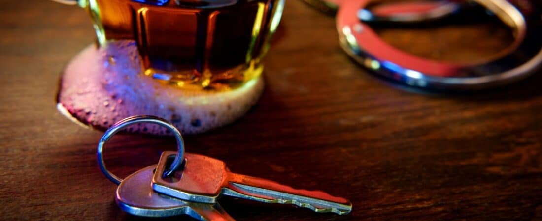 Handcuffs with a spilt beer and car keys on a table.