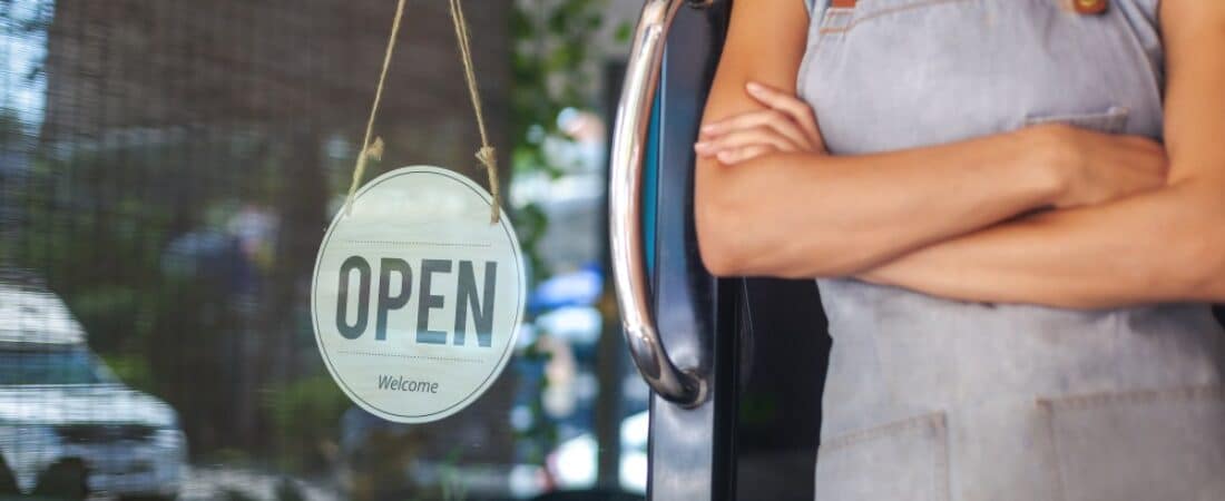 Small business owner standing by a door that has an open for business sign hung.