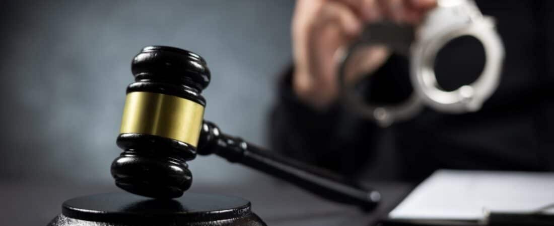 A man holding up handcuffs with a gavel in the foreground.